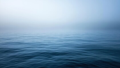Obraz premium Calm blue ocean waters under a misty sky at dawn near the shoreline