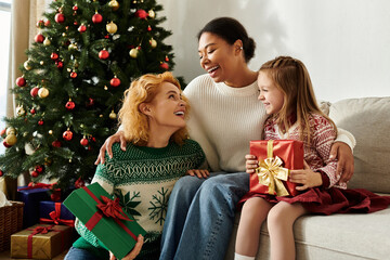 A beautiful couple shares laughter while giving their daughter Christmas gifts by the tree.