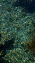 The water is clear and calm, with ripples and reflections of the sky and rocks
