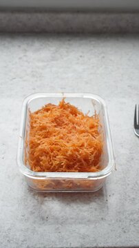 Hands opening a plastic container with grated carrots and eating with a fork