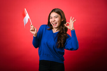 An Asian woman enthusiastically holds the Indonesian flag in her right hand while making an 