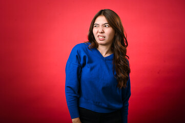 An Asian woman wearing a blue sweater is grimacing, displaying an uncomfortable or disgusted facial...