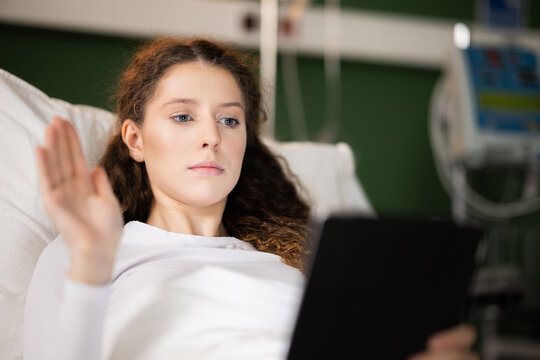 Beautiful young female patient holds tablet in hands has video caht with family.