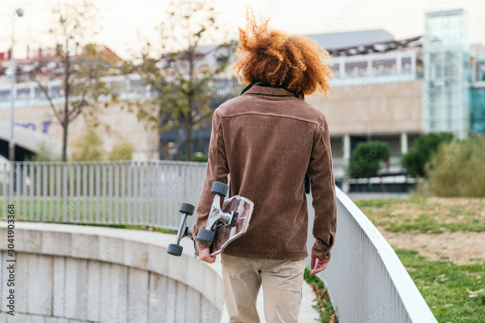 Wall mural stylish young man walking with longboard in the city