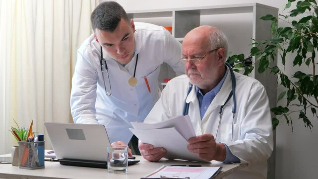 An elderly doctor in the office, talking with a young intern doctor, discussing the patient's condition and his further treatment, through discussion they come to a consensus regarding the diagnosis a