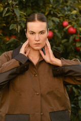 A beautiful girl in a brown autumn jacket in an apple orchard. A fashionable girl at a fashion show in an apple orchard