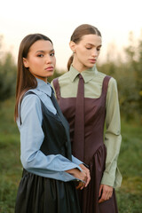 Two stylish girls in dresses with ties in the summer garden. Fashion show in nature