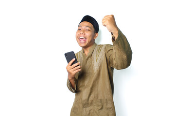 joyful asian muslim man wearing islamic dress show winning gesture with holding mobile phone isolated on whtie background