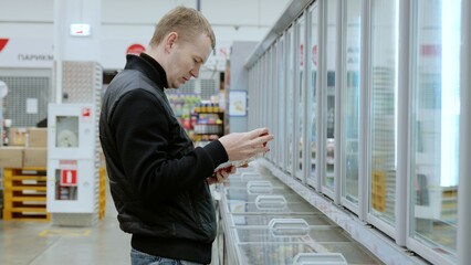 Shopper examining the packaging of a frozen food item in the supermarket before deciding to buy. A...