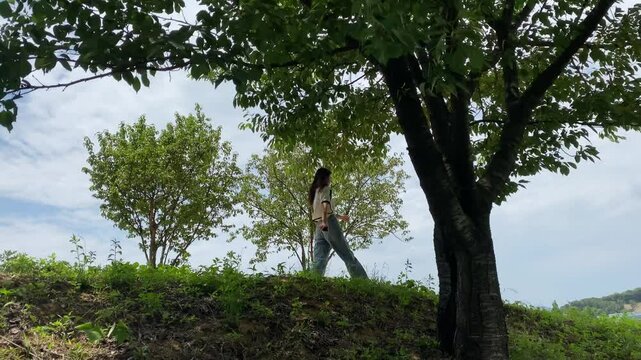 An asian girl is walking in a forest hill in korea. The sky is cloudy and the trees are green. Peaceful like a movie