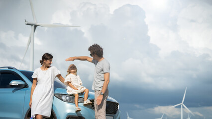 Happy family enjoying their time at a wind farm in an electric car From wind turbine generators to charging stations Clean, renewable energy from wind turbine generators