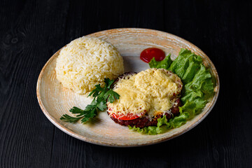 cutlet with tomatoes and cheese, side dish boiled rice, fresh herbs. on a black wooden background
