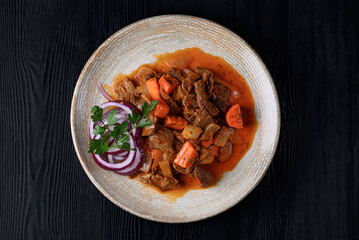 roast meat with vegetables in juice, fresh onions. on a black wooden background