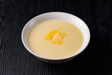 corn porridge with milk and butter. on a black wooden background