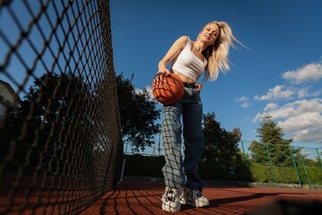 Sportswoman siting on tennis court with a basketball ball