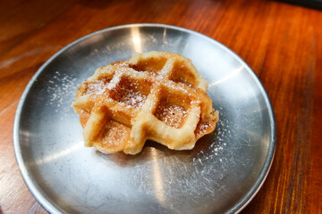 close up of freshly baked Belgium waffle on a metal steel plate with sugar powder