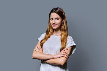 Fototapeta premium Beautiful young girl with crossed arms looking at camera on gray background
