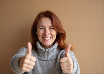 Redhead woman with joyful smile giving thumbs up against beige background