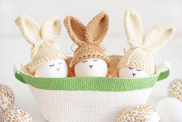 Easter eggs in crochet knitted hats with rabbit ears in nest. Easter celebration concept