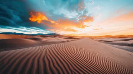 Naklejka premium A desert landscape with a beautiful orange and pink sky. The sky is filled with clouds and the sun is setting. The scene is peaceful and serene