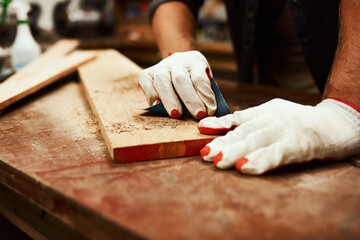 Carpenter, hands and wood sandpaper for workshop, maintenance and contractor project. Person, tools and builder gloves for protection with home construction, repair and sanding plank at carpentry © Malambo/peopleimages.com