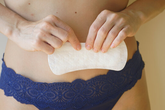 Feminine hygiene: girl in panties gently holding one daily pad with her fingers, close-up. Products for maintaining cleanliness during menstruation.