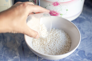 Cooking rice in a rice cooker. The woman measures out a cup of rice and pours it into a cup