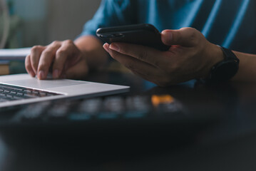 Individual holding a smartphone in one hand while typing on a laptop with the other.