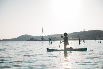 A man is surfing on a sap board on calm water at sunset.