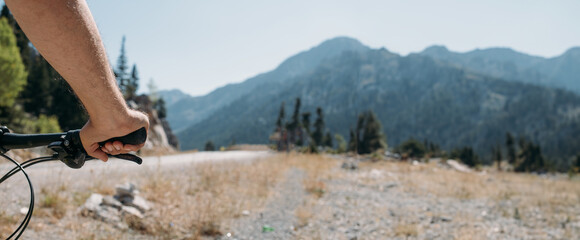 Naklejka premium Close-up of a man's hand on the handlebars of a bicycle against the background of mountains.
