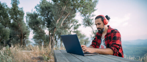 A young man is working on a laptop at a camping site in the mountains.