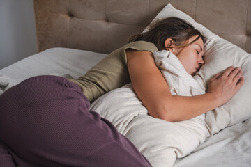 Woman peacefully sleeping with pillow in cozy bedroom setting.