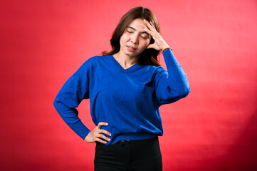 An Asian woman with brown hair, wearing a blue sweater, appears frustrated or in pain. She is...