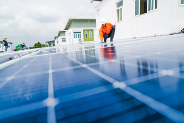 A worker in an orange safety jacket inspects solar panels on a rooftop, using a laptop to ensure...