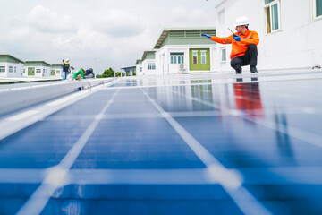 A worker in an orange safety jacket inspects solar panels on a rooftop, using a laptop to ensure...