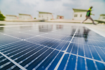 A close up of solar panels with a worker blurred in the background. The focus on the panels emphasizes the importance of renewable energy technology and solar power installations.