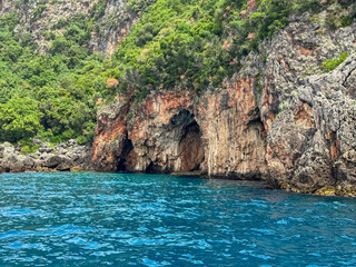 Boat trip with scenic view of large sea cave called Monastery caves near Himare, Vlore, Albania. Dramatic coastal landscape of Albanian Riviera with natural archway. Sightseeing on Mediterranean sea