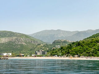 Panoramic view of the picturesque coastline of coastal tourist town Himare, Vlore, Albania. Boat tour with scenic vistas of Himare castle on hilltop surrounded by majestic mountains. Summer vacation