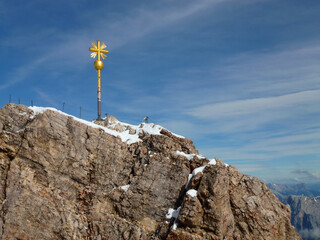A picturesque view of the iron yellow cross installed on the mountain against the background of the blue sky. Mountain peak in Bavaria, Germany