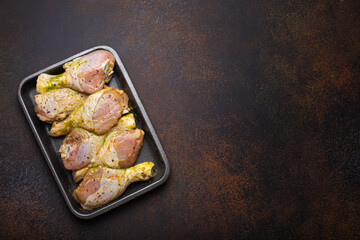 Raw uncooked chicken legs in green marinade with seasonings in black plastic container top view on dark rustic background. Preparing healthy meal with marinated chicken drumsticks, copy space.