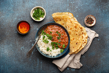 Traditional Indian Punjabi dish Dal makhani with lentils and beans in black bowl served with basmati rice, naan flat bread, fresh cilantro and spoon on blue concrete rustic table top view.