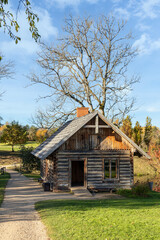 An old traditional bathhouse. A log building with a wooden tile roof. Small wooden cabin with chimney in rural autumn landscape