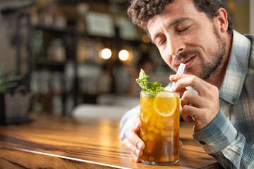 Close-up young man enjoying a piña colada tea cocktail with peach balls, orange or lemon slice and mint, non-alcoholic cocktail, refreshing and healthy drink, free background to write, copy space