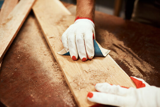 Carpenter, hands and wood sandpaper for handyman work, maintenance and contractor project. Person, tools and builder gloves for protection with home construction, repair and sanding at carpentry