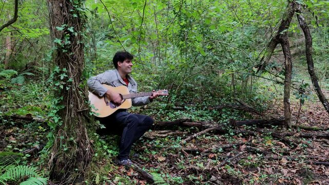 Young hiker playing acoustic guitar in the forest, relaxing in nature