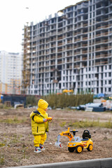 Child playing with toy excavator on the background of house under construction