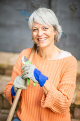 Smiling senior woman holding pruning shears and rake while gardening
