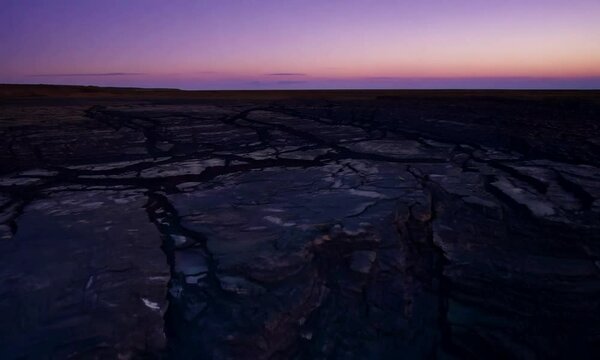 Tracking shot with twilight hues: The camera starts by focusing on a close-up of an earthquake fault, showing the disruption in the earth&rsquo;s surface. It then tracks back to reveal the broader fault zon