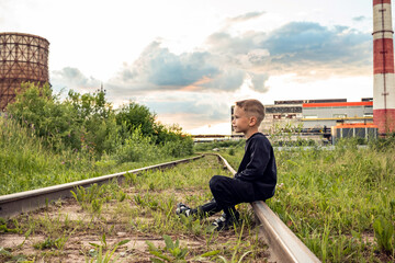 Boy on a railway with a factory in the background.