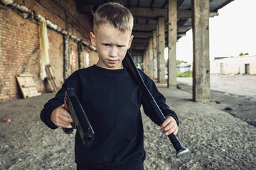 A boy in black clothes with a baseball bat and a gun in his hands.